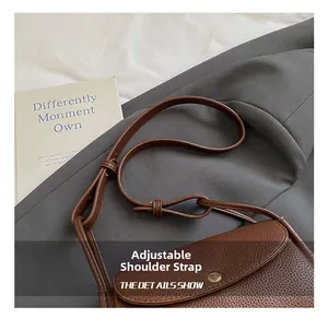 Detail of adjustable shoulder strap and litchi grain leather on a brown crossbody bag