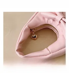 Detail of pink bow handbag featuring soft faux leather texture and golden heart zipper
