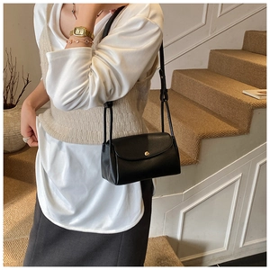 Detail of black litchi grain leather bag with golden magnetic buckle on woman's shoulder