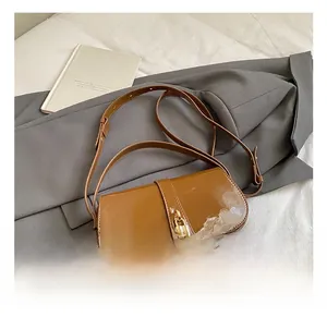 Close-up of brown patent leather underarm bag with gold padlock on a gray blazer