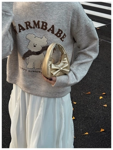 Close-up of metallic gold bow handbag held by child in grey sweatshirt and white skirt