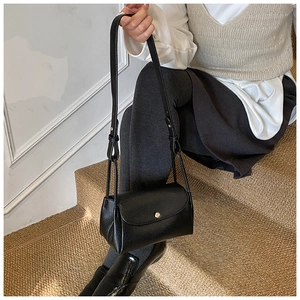 Detail of black pebbled leather texture on minimalist shoulder bag with gold metal buckle