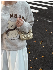 Detail of a champagne gold bow handbag held by a girl wearing a grey puppy sweatshirt