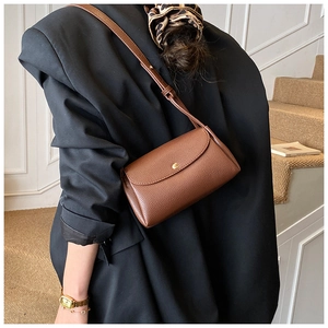 Detail of dark brown pebble leather bag with golden round buckle worn by a model