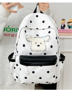 Détail d'un sac à dos d'école blanc à pois avec écusson chiot en peluche 3D et nœud bleu