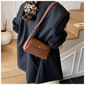 Close-up of brown litchi pattern leather bag with gold buckle on black blazer