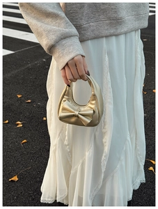 Golden mini bow handbag for girls held by model in an urban lifestyle outdoor setting