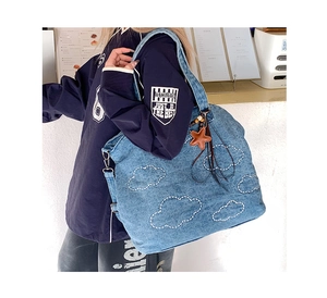Detail of large denim shoulder bag with white stitched cloud patterns and star pendant