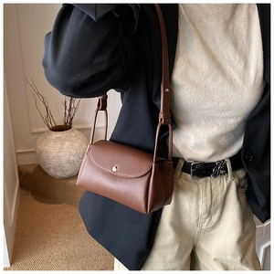 Detailed view of a brown pebbled leather crossbody bag with a gold round metal snap buckle