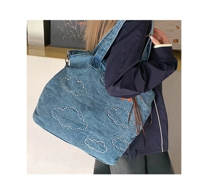 Detail of a large denim tote bag with white cloud embroidery for casual daily use