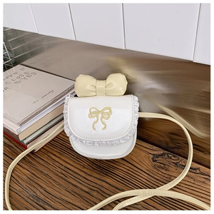 Detail of white girls' crossbody bag with yellow bow embroidery and lace trim on wood