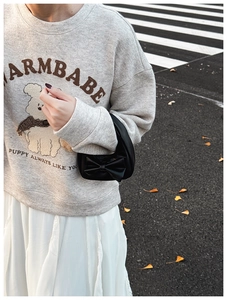 Detailed view of a mini black handbag with bow decoration held against a white skirt