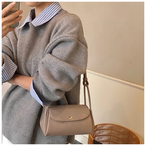 Close-up of khaki pebbled leather shoulder bag featuring a gold round buckle and knot strap