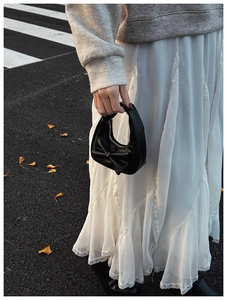Detail of a black leather handbag with a bow decoration on a white lace dress backdrop