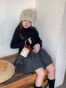 Detail einer beige gesteppten Beuteltasche mit roter Schleife und Goldkette auf Holzbank