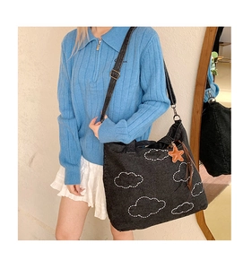 Detail of black denim tote bag featuring white cloud embroidery and a star leather pendant