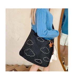 Detail of black denim tote bag with white cloud embroidery and orange star charm