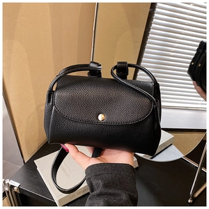 Detail of black lychee grain leather handbag featuring a round golden metallic buckle