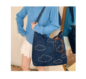 Detail of denim tote bag with cloud embroidery, leather tassels and adjustable strap