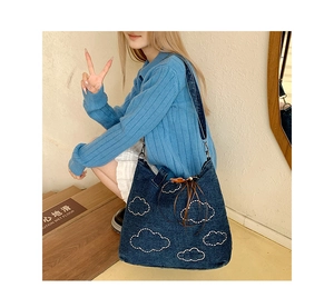 Detail of blue denim tote bag with white cloud patterns and metal hook attachment