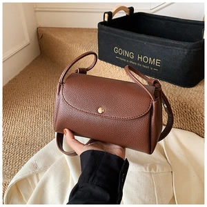 Close-up of brown lychee grain leather handbag with gold metal buckle held in hand