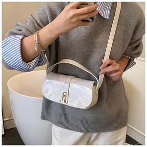 Close-up of a white patent leather shoulder bag with a gold buckle and adjustable strap