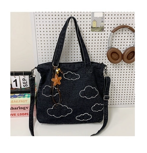 Detail of black denim tote bag with cloud embroidery and star charm on pegboard