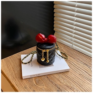 Mini schwarze Steppbeuteltasche mit roter Schleife und Goldkette auf Holztisch