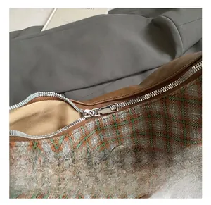 Detail view of half-moon plaid bag with silver zipper and brown leather trim