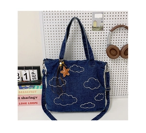 Detail of dark blue denim tote bag with white cloud embroidery and orange star charm