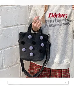 Detail of black denim bucket bag with purple pom-poms and gold metal hardware hooks