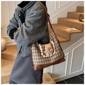 Detail of plaid crossbody bag featuring a cute plush bear and brown leather base