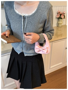 Close-up of pink satin handbag with large bow detail held by girl in knit cardigan