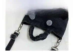 Close-up of denim tote bag featuring gray plush pom-poms and vintage metal hardware