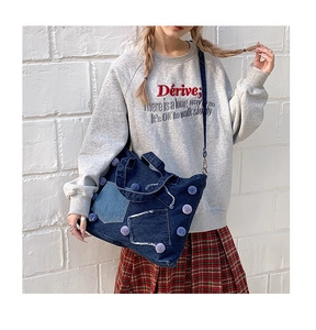 Dettaglio della borsa in denim blu scuro con pompon viola e tasche con bordi a vivo