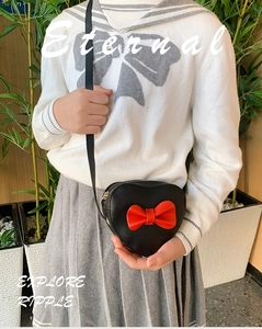 Detail of heart-shaped girl crossbody bag with red bow and gold zipper on leather