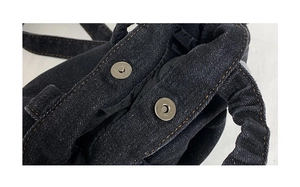 Detail of dual magnetic snap buttons on dark denim bucket bag with contrast stitching