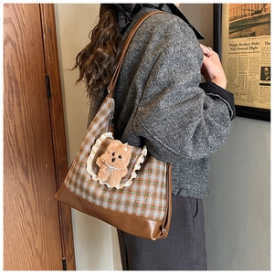 Detail of checkered shoulder bag featuring a plush bear charm and white lace trim