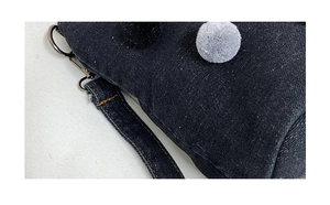 Detail of denim bucket bag with plush pom-poms, D-ring hardware and contrast stitching