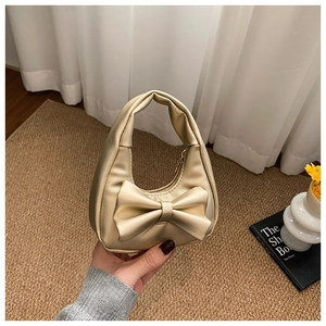 Close-up of golden mini handbag featuring a large bow and premium pebbled texture