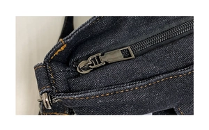 Dettaglio della borsa in denim blu scuro con cuciture arancioni e cerniera in metallo