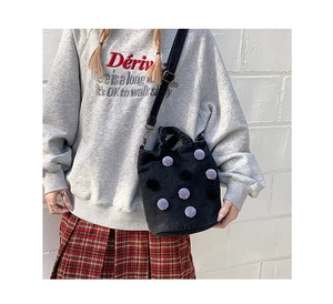 Detail of black denim bucket bag with plush pom-poms and adjustable shoulder strap