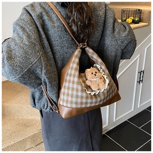 Detail of checkered kid shoulder bag featuring a plush bear charm and adjustable strap