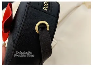 Detail of black leather kid's bag with red bow, gold zipper, and detachable strap