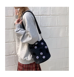 Close-up of black denim bucket bag with purple plush polka dots and wide strap