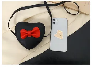 Detailed top view of a mini black heart purse with red bow next to a smartphone