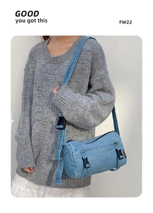 Détail d'un sac bandoulière cylindrique en jean bleu avec boucles noires et sangle large