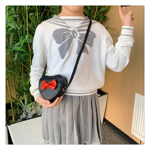 Detailed view of child wearing heart-shaped crossbody bag with red bow decoration