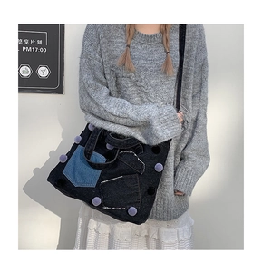 Vista dettagliata della borsa tote in denim nero con tasche patchwork blu e pompon viola
