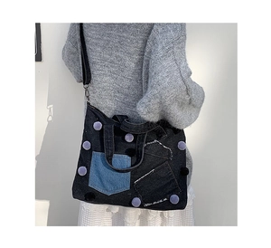 Dettaglio borsa in denim con patch blu, pompon viola e tracolla regolabile e rimovibile